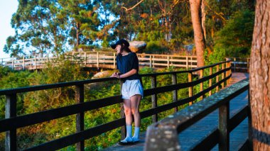 Şapka takmış genç beyaz bir kız ahşap bir geçitten manzarayı izliyor.