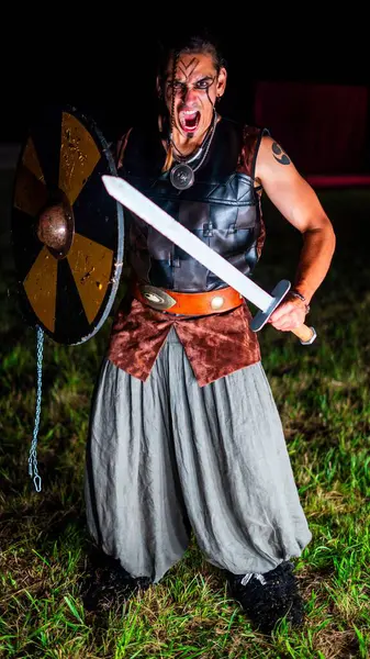 Angry Viking warrior with black war paint, openig his mouth and holding his sword.