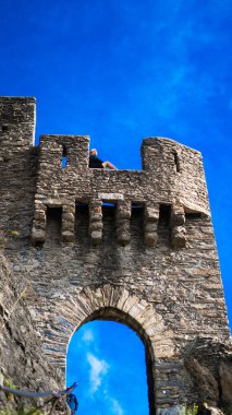 Şatonun duvarında oturan genç bir adam. Güneşli bir gün, mavi gökyüzü. Dikey fotoğraf