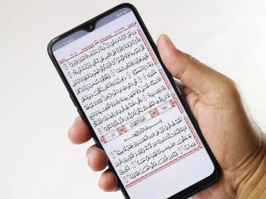 İçinde Kuran uygulaması olan el ele tutuşan cep telefonu. Al-Kahfi Sûrası üzerine Kur 'an.