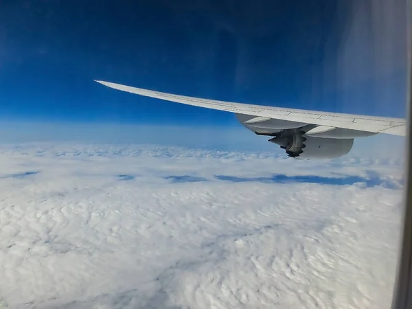 青い空と白い雲の上の飛行機からの眺め 飛行機に乗って飛んでいる 空の雲の上を飛んで飛行機の翼 楕円形の窓 イルミネーター — ストック写真