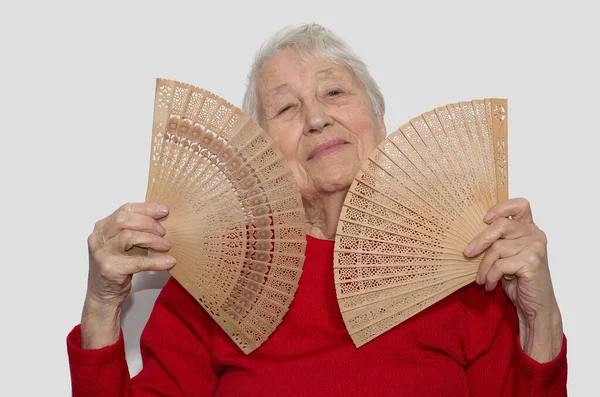 The old woman cooling off with a fan in her hand. Studio shot isolated on white