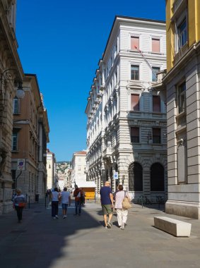 Trieste, İtalya - 1 Ekim 2023: İnsanlar eski ve renkli Akdeniz evlerinin cepheleriyle Trieste sokaklarına dökülüyor. Trieste, İtalya