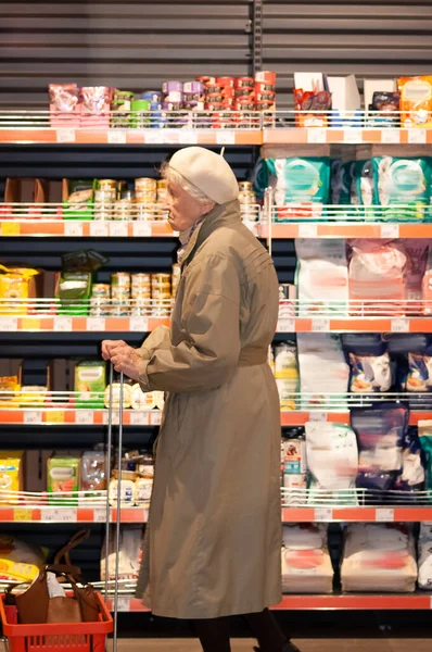Senior old female is shopping at a grocery store. She is reading nutrition facts on the label. She is shopping alone.