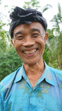 Ubud, Bali - 12 Ocak 2025: Geleneksel bir şapka takan ve kameraya bakan bir çiftçi.