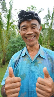 Ubud, Bali - 12 Ocak 2025: Geleneksel bir şapka takan ve kameraya bakan bir çiftçi.