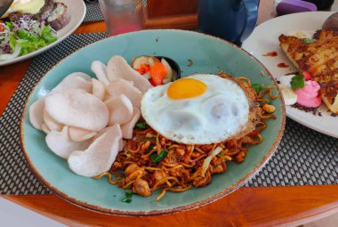 Ahşap masada servis edilen yumurta, sosis ve köfte soslu kızarmış şehriye.