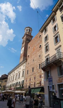 Verona, İtalya - 12 Mayıs 2025: İnsanlar İtalya 'nın Verona kentindeki ortaçağ duvarının balkonunda çiçeklerle geleneksel İtalyan binalarının yakınına gidiyorlar