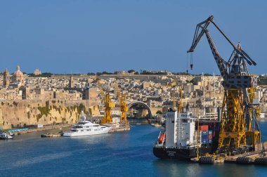 Valletta, Malta - September 24, 2025: Cargo cranes and large ship atlantic silver docked near fortifications and boats in the harbor.