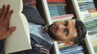 Dikey Ekran: Gözlüklü sakallı adam kitaplığın yanında duruyor ve kitap okuyor, sayfaları çeviriyor, edebiyattan zevk alıyor. Kütüphanede düşük açı okuyucusu. Bilgi kavramı