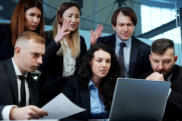 Business people gathering together in front of laptop in office and looking tense, checking online data on stock market, gesturing with disappointment and making sad faces. Concept of failure