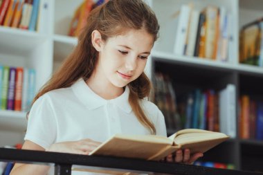 Beyaz polo tişörtlü gülümseyen çocuk metal korkulukların yanında duruyor ve kitap okuyor, arkasında kitaplıklar var. Ark, edebiyattan hoşlanan zeki bir kızı okul kütüphanesinde vurdu. Eğitim kavramı