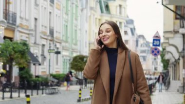 Neşeli esmer kadın, günlük kahverengi palto giyen, telefonla konuşan, eski bina geçmişini bulanıklaştıran. Şehirdeki genç bir kadının görüntüsü. İletişim kavramı