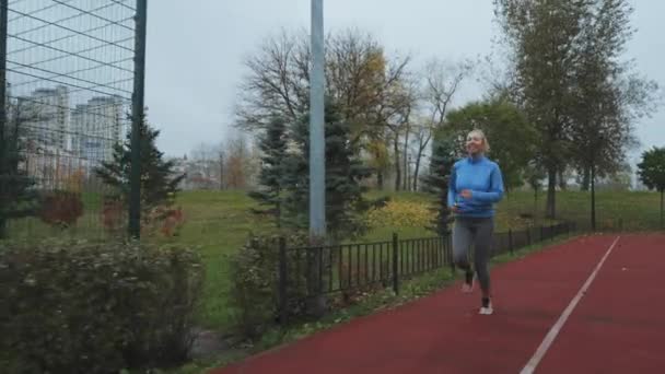 Młoda Blondynka Niebieskiej Sportowej Kurtce Biegająca Torze Jesienią Rano Namierzam — Wideo stockowe