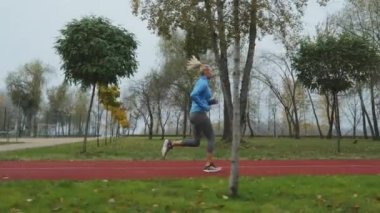 Sonbahar parkında mavi spor ceket giymiş yavaş çekim formundaki kadın yerde yatan yapraklar. Sabahki aktif insan eğitiminin görüntüsü. Zindelik kavramı