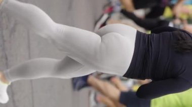 Dikey Ekran: Ağır çekim şişman kadın siyah spor ceket giyiyor ve şehir yolunda diğer insanlarla birlikte koşan beyaz tozluklar, elinde akıllı telefon. Maraton yarışmacılarının kısmi görünümü