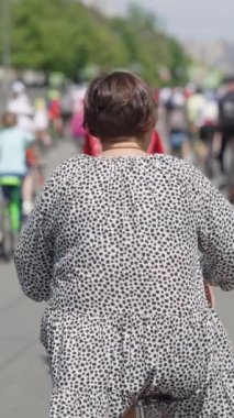 Dikey Ekran: artı uzun boylu kadın yavaş çekimde bisiklet sürüyor, yanında bisiklet süren bir sürü insan var. Şehirdeki spor müsabakalarının çekim yarışmacıları. Sağlıklı yaşam tarzı kavramı
