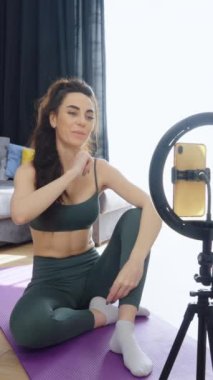 Dikey Ekran: Spor giyim bölümündeki kadın tripodlu akıllı telefonlu, neon yüzüklü ve boynu için egzersiz yapan video kaydı yapıyor. Spor blogcusu karantinada kalırken evden yayın yapıyor