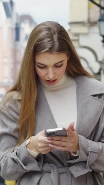 스크린 스마트폰으로 온라인상에서 코트를 코트를 아름다운 금발의 꿈만같은 거리에서 수다나떨고 — 비디오