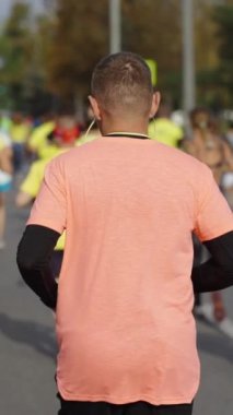 Dik ekran: yavaş çekim adam spor giyer ve diğer insanlarla birlikte şehir yolunda çalışan kulaklıklar takar. Maraton yarışmacılarının çekimleri devam ediyor. Sağlıklı yaşam tarzı kavramı