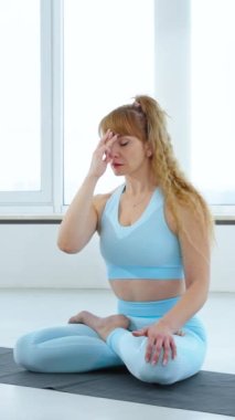 Mavi spor kıyafetli bir kadın burun ya da burun delikleri egzersizi ya da Lotus pozunda nadi shodhana yapıyor. Yogi kadın yoga stüdyosunda Anulom-Vilom Pranayama çalışıyor. Sağlıklı yaşam tarzını kabul et