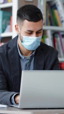 Koruyucu maske takan bir adam kütüphanede dizüstü bilgisayarla çalışıyor, internette geziniyor, baş ağrısı çekiyor ve şakaklara masaj yapmaya başlıyor. Hastalık belirtileri