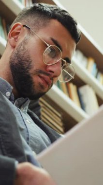 Dikey Ekran: Gözlüklü genç sakallı adam kütüphanede kitap okurken, sayfaları çevirirken, edebiyattan zevk alırken. Okuyucu ilginç bir hikaye anlatıyor. Eğitim kavramı