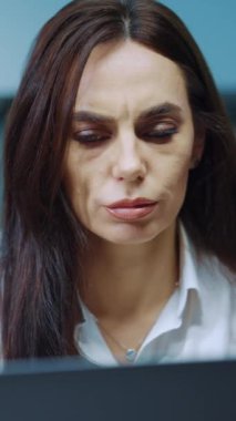Vertical Screen: Businesswoman with long hair and makeup wearing white shirt working at laptop and nodding head receiving message with bad news. Frustrated manager in office. Concept of stress
