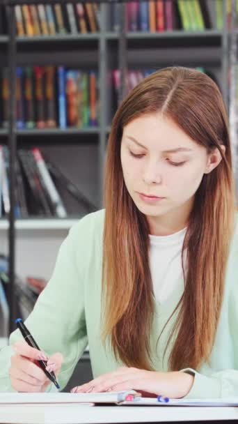 垂直屏风 白人女生在图书馆学习 停止写作 从相机后面看窗外 模糊的书架背景 教育的概念 — 图库视频影像