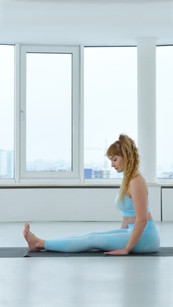 縦画面 床ヨガスタジオに立って足を上げることによって若いブロンドの女性のトレーニング腹筋 ヨギ女はヨガを練習し 手でバランスを取り 練習をする 健康的なライフスタイルのコンセプト — ストック動画