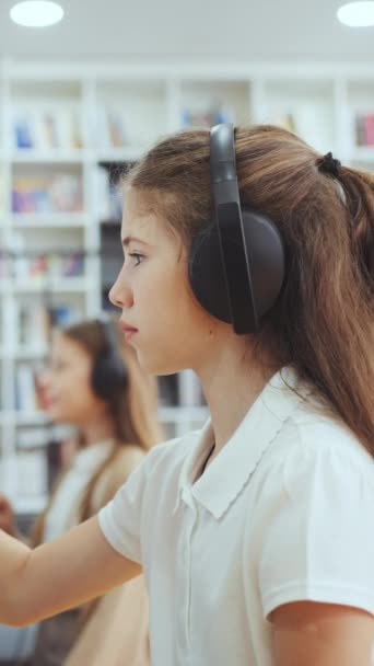 垂直屏风 学生们穿着耳机坐在课堂上 并使用与墙壁相连的装置 触摸屏幕 另一个孩子在后面 侧观在学校学习的儿童 教育的概念 — 图库视频影像