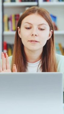 Vertical Screen: Teen girl waving hand talking to camera. Caucasian teenager recording vlog, streaming for social media, video calling in online chat on laptop. Online course. Distance learning