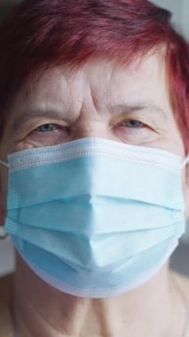 Vertical Screen: Senior woman with short hair looking at camera and taking off medical mask, closeup of wrinkled face. End of lockdown. Concept of healthcare