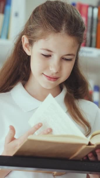 垂直屏风 穿着白色马球衫 站在金属栏杆旁边看书的笑孩子 Arc在学校图书馆拍摄了一个聪明的女孩欣赏文学 教育的概念 — 图库视频影像