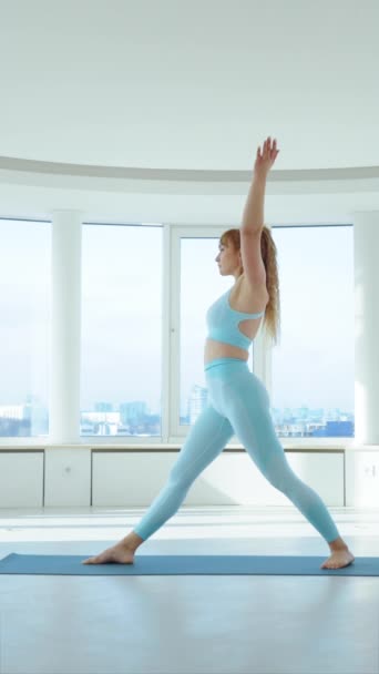 垂直屏风 适合成年女子在演播室练习三角裤变奏的瑜伽序列 Yogi的女性做的是背景为全景窗的Trikonasana 健康生活方式概念 — 图库视频影像