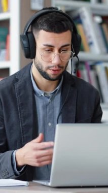 Dikey Ekran: Gözlüklü genç ve başarılı bir adam dizüstü bilgisayarının önünde oturuyor ve kafasında kulaklık, video çağrısı var. Uzaktan çalışan bir iş adamı. Öğrencilere uzaktan eğitim veren öğretmen