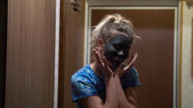 Yüzünde çamur maskesi olan at kuyruklu güzel sarışın ergen evde dans edip eğleniyor. Kozmetik ameliyatlarından hoşlanan neşeli ergenlik çağındaki kadın portresi. Cilt bakımı kavramı