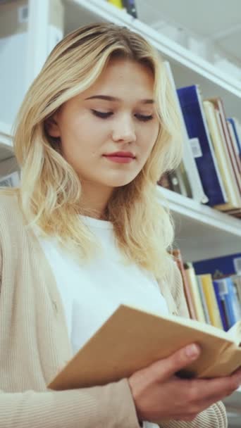 垂直屏风 穿着休闲装的金发少女站在书架上看书 女学生在学习 读者喜欢图书馆里的畅销书或古典小说 教育的概念 — 图库视频影像