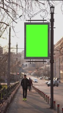 Dikey Ekran: yeşil ekranlı reklam panosu şehir trafiği arka planı. Bulanık araç yolda ilerliyor. Kaldırımdaki yayalar, reklam lambasının altından geçiyorlar ve şehir yolu boyunca araba sürüyorlar.