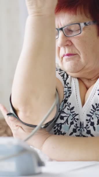 Vertical Screen Seniorin Mit Brille Setzt Manschette Des Blutdruckgeräts Auf — Stockvideo