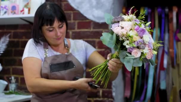 スタジオで結婚式の花束ではさみでプロの花屋の切断花茎 エプロンの白人女性のマスターは 花の組成を作成します フロリストリー ハンドメイド スモールビジネスのコンセプト — ストック動画