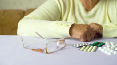 Evdeki masada ilaç ve gözlüklü yaşlı kadın elleri var. Yaş, ilaç, sağlık, tedavi, emeklilik, insan kavramı