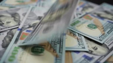100 dolarlık banknotlar bir tomar para içinde dönen masanın üzerine düşüyor. Ek banknotlar yağdıkça daha da büyüyen bir yığın para. İş ve finans kavramı