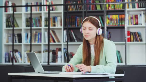 Valkoihoinen Koulutyttö Yllään Kuulokkeet Haaveilee Istuessaan Pöydässä Hänen Kannettava Tietokone — kuvapankkivideo