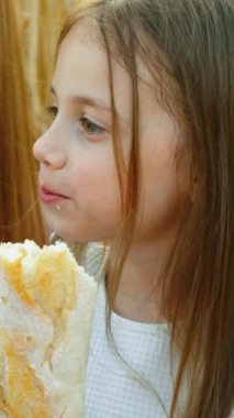 Dikey Ekran: Buğday tarlasında piknikte ekmek yiyen küçük bir kız. Mutlu çocuk gün batımında kırsalda yemeğin tadını çıkarıyor. Aile kavramı