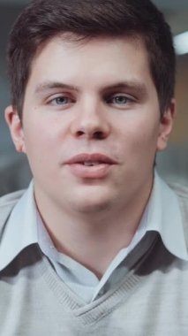 Dikey Ekran: Gömlek ve kazak giyen genç işadamı ofiste oturuyor ve online görüşme yapıyor, web kamerasıyla partneriyle konuşuyor. Şirket ilerlemesi hakkında rapor veren yöneticinin kapatılması