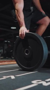 Bir elinde 15 kilo halter plaka taşıyan ve koyu renk spor salonundaki halterin üzerine koyan vücut geliştirici. Güçlü bir sporcunun egzersiz için ekipman hazırlarken ki görüntüsü. Spor anlayışı