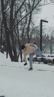 Spor giyimli bir adam, kış parkında egzersiz yapan, bacağını esneten ve yere eğilen bir şapka ve eldiven. Atletizm antrenmanının kavisli çekimi. Spor anlayışı