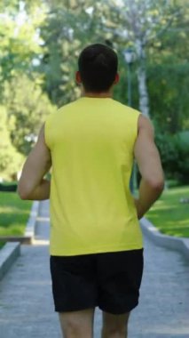 Dikey Ekran: Atletik adam sarı gömlekli ve siyah şortlu sabah parkta koşuyor. Atış talimini takip eden koşucu yazın dışarıda egzersiz yapıyor. Zindelik kavramı