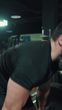 Dikey Ekran: Siyah spor giyimli kaslı adam spor salonunda halterle egzersiz yapıyor, diğer sporcular bulanık arka planda. El bilgisayarı vücut geliştirici. Spor anlayışı